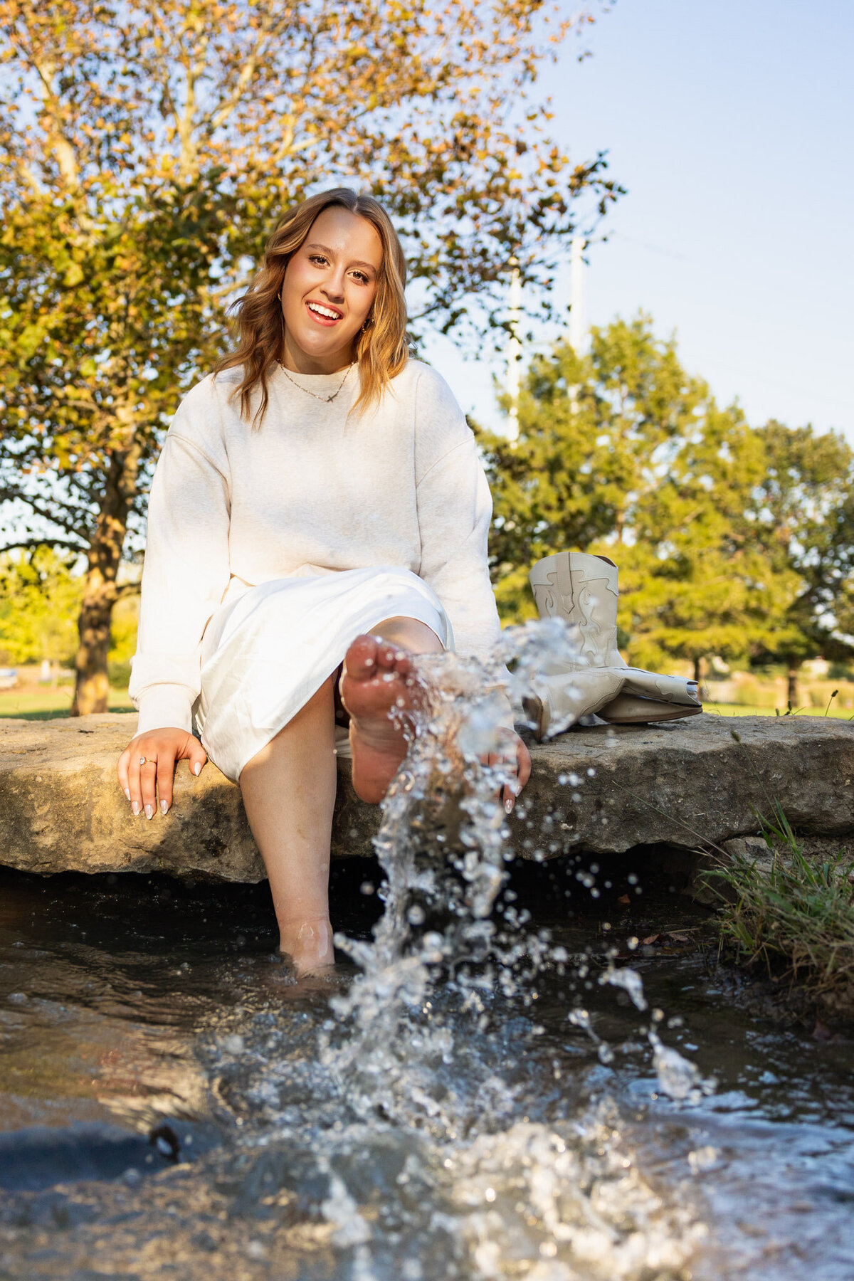 Senior girl splashing water with her feet at a creek during fall session in Lawrence KS