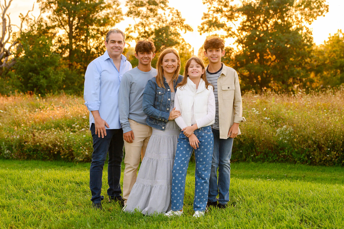 Mom and dad with their teenage son and daughter wearing blue and white sitting in front of the Golden sun setting for their Burlington, ON family photography session