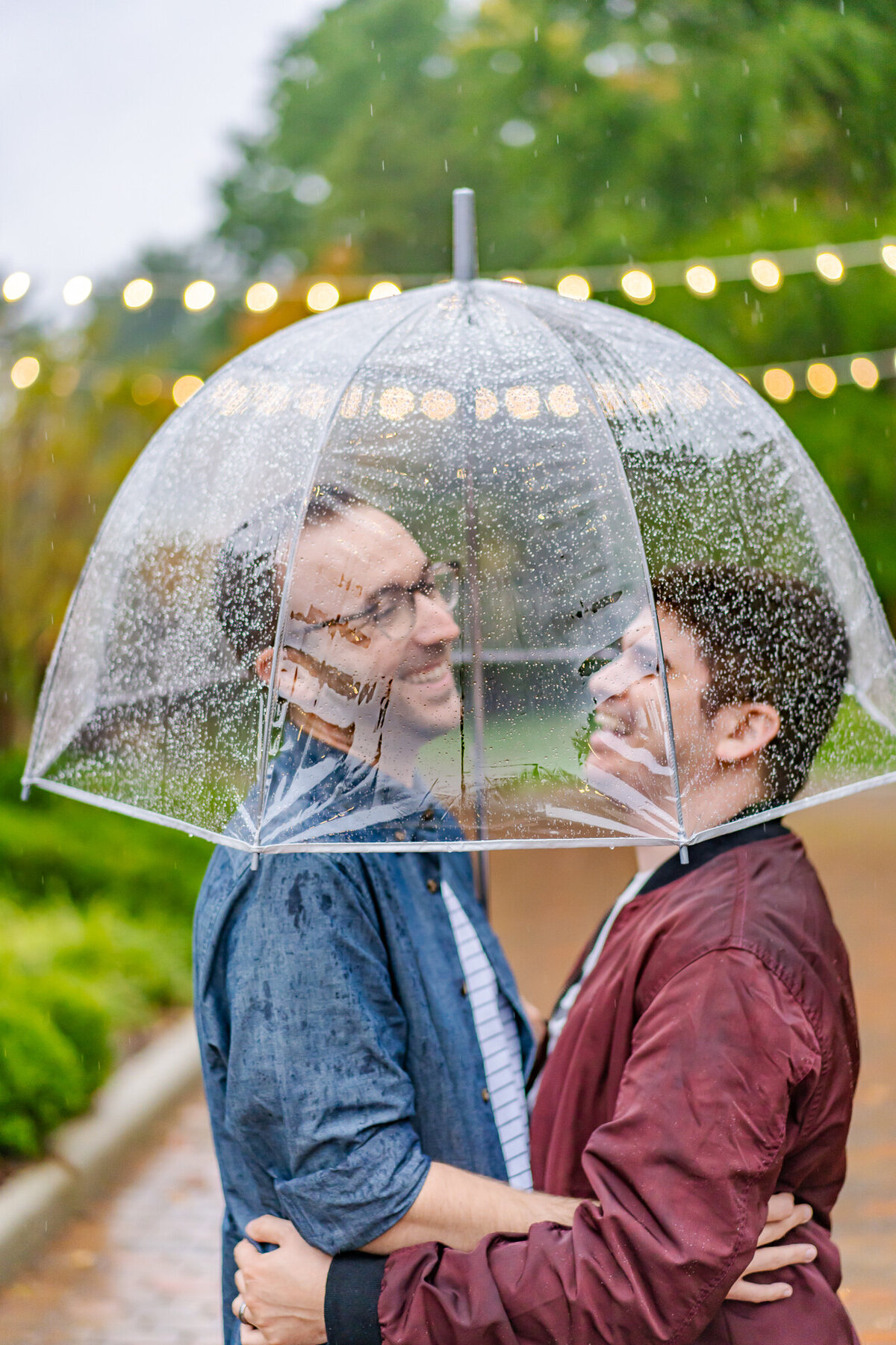 Engaged LGBTQ+ couple, Doug and Shawn, hold each other and laugh under a clear umbrella in the rain at Jeffrey Mansion in Columbus Ohio.