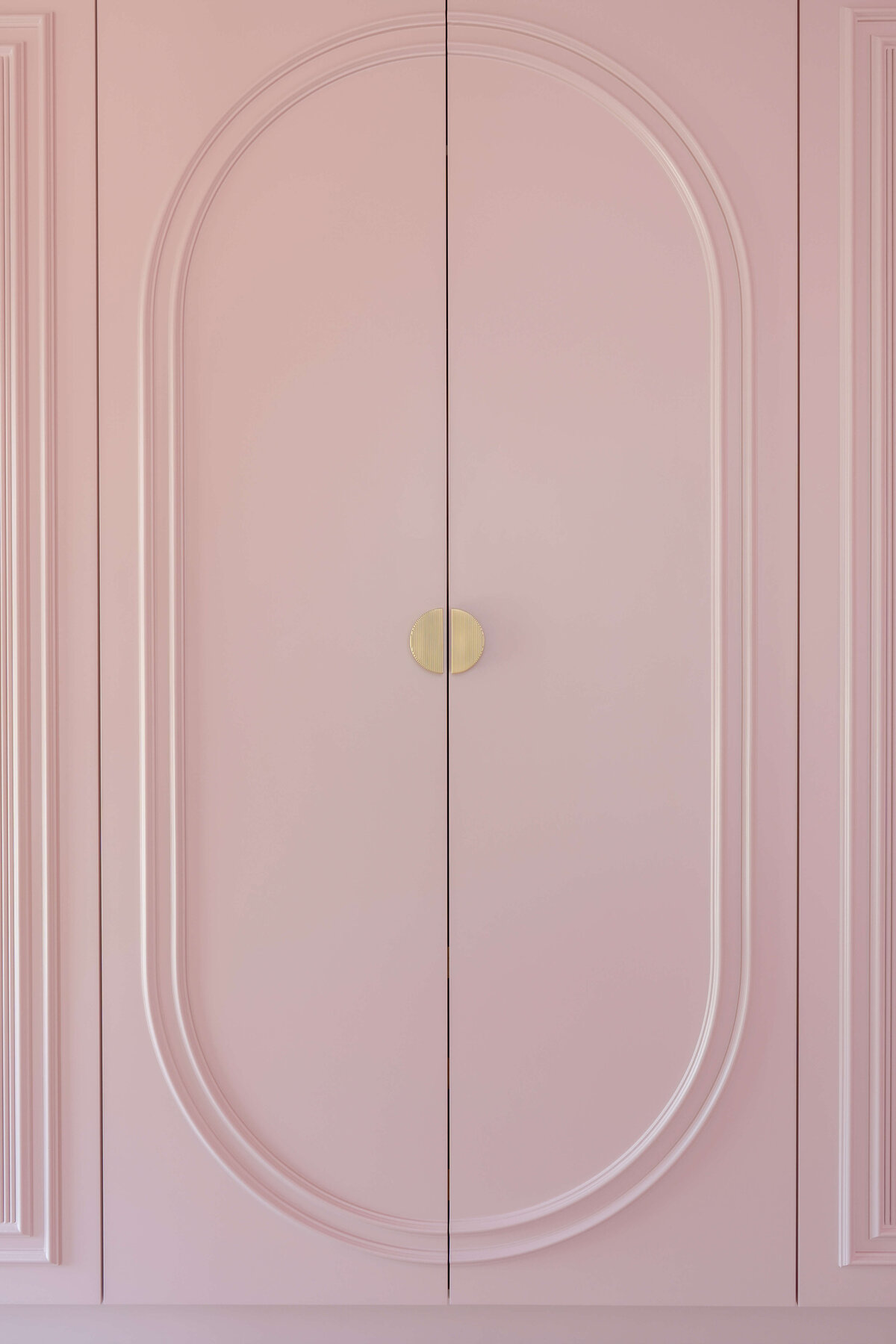 Built-in closets in a girl's pink bedroom. The closets are pink with intricate molding and gold handles.