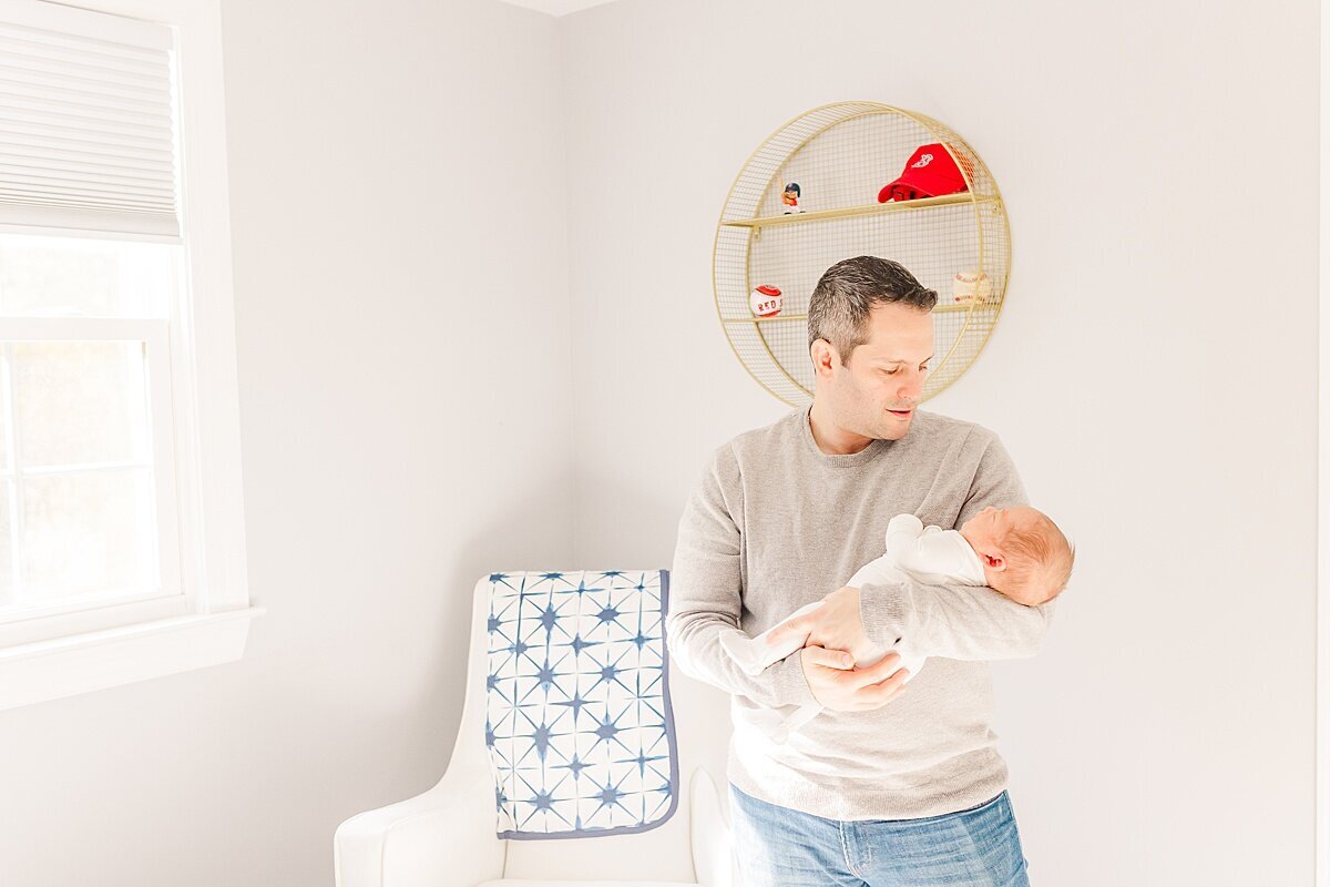 dad holds ababy  during in home newborn photo session with Sara Sniderman Photography in Sherborn Massachusetts