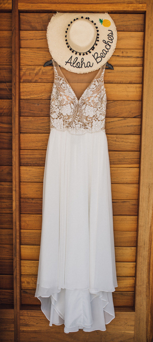 Brides dress hanging on wooden shutters with an aloha beaches sunhat above