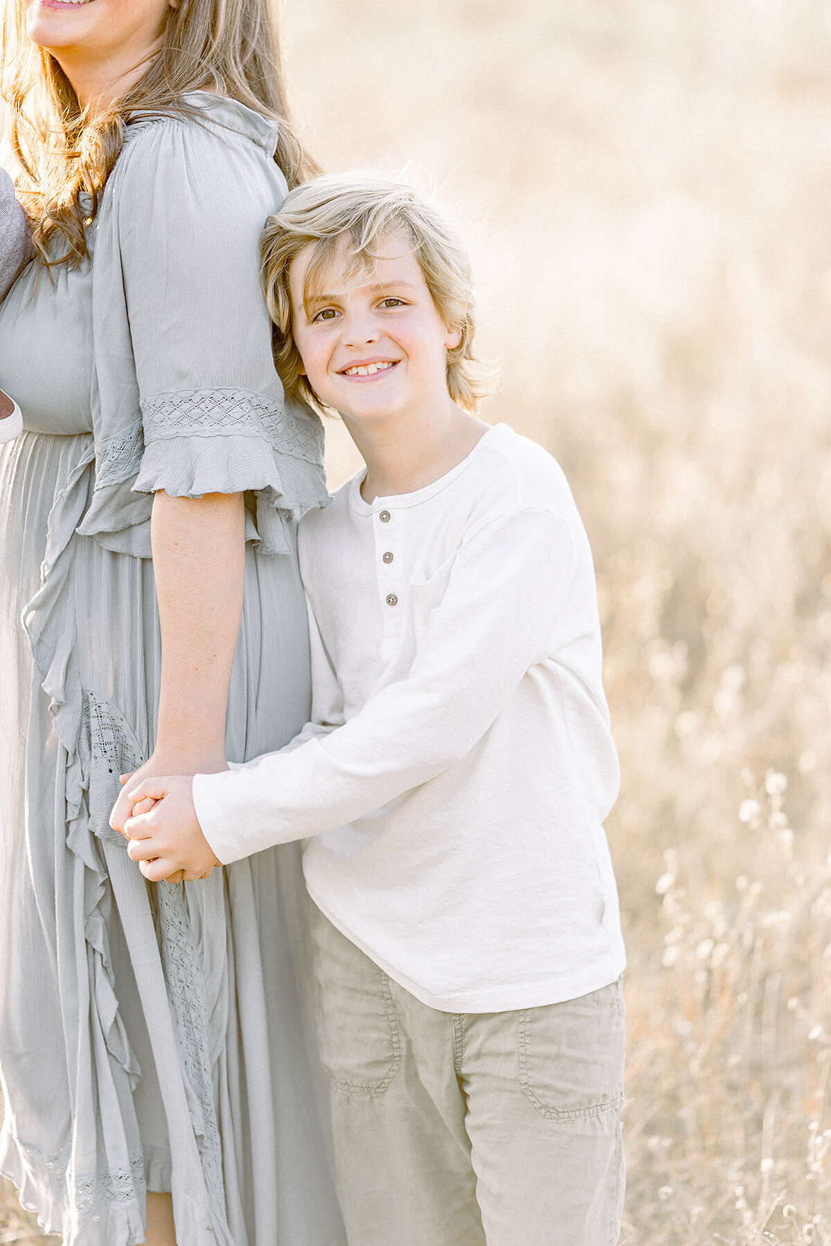 Photo of a young boy holding his mothers hand while he looks at his family photographer smiling.