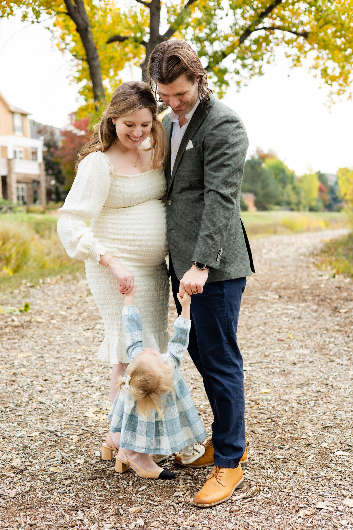Mom and dad hold each other close and their toddler daughter holds their hands and swings. 