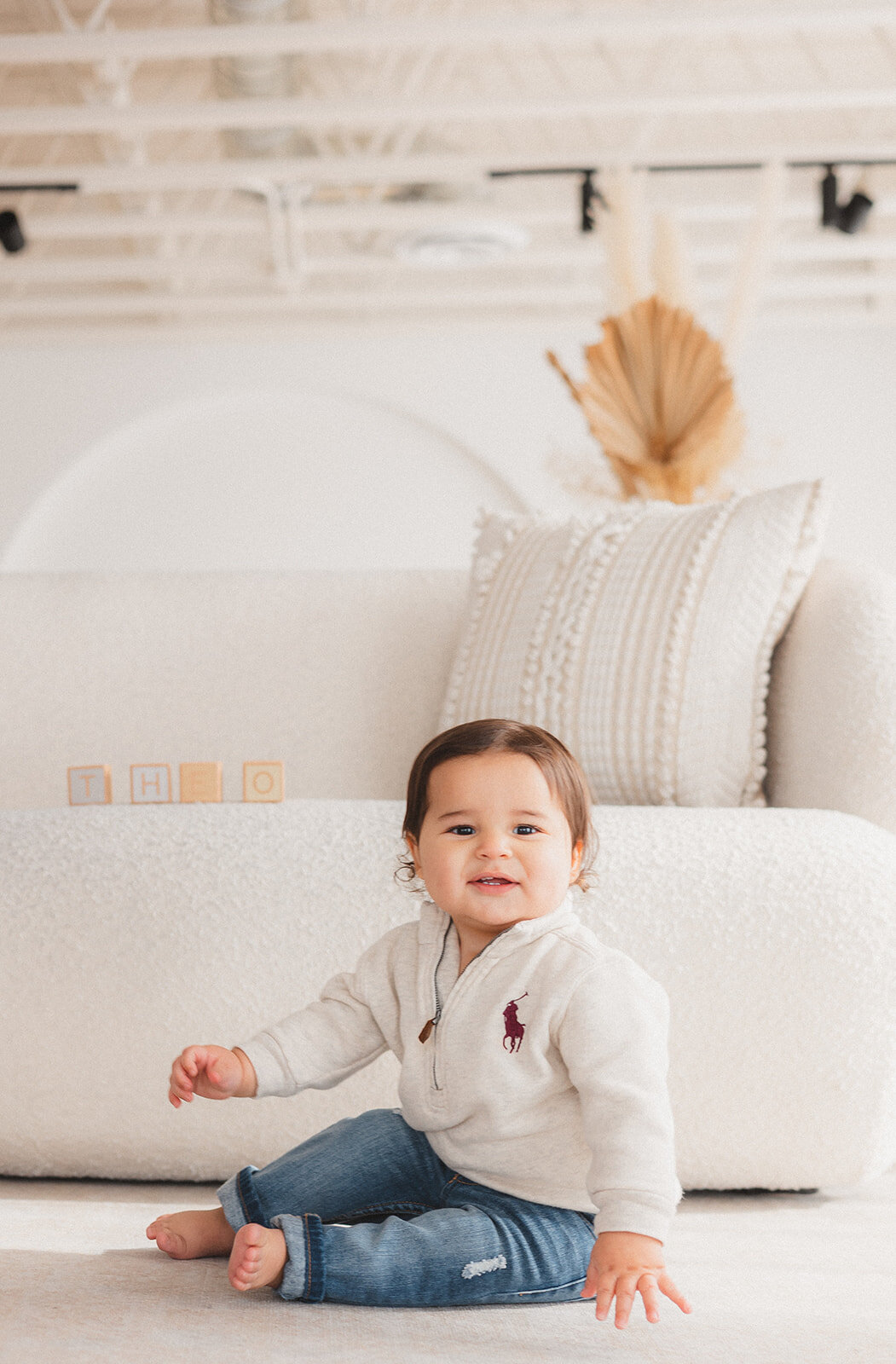 A baby boy smiles in front of a couch.
