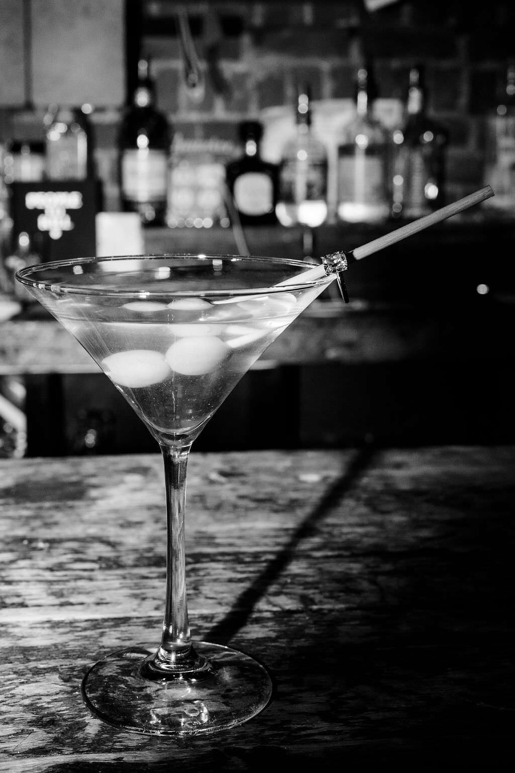 black and white photo of a martini glass with two olives in it on a bar