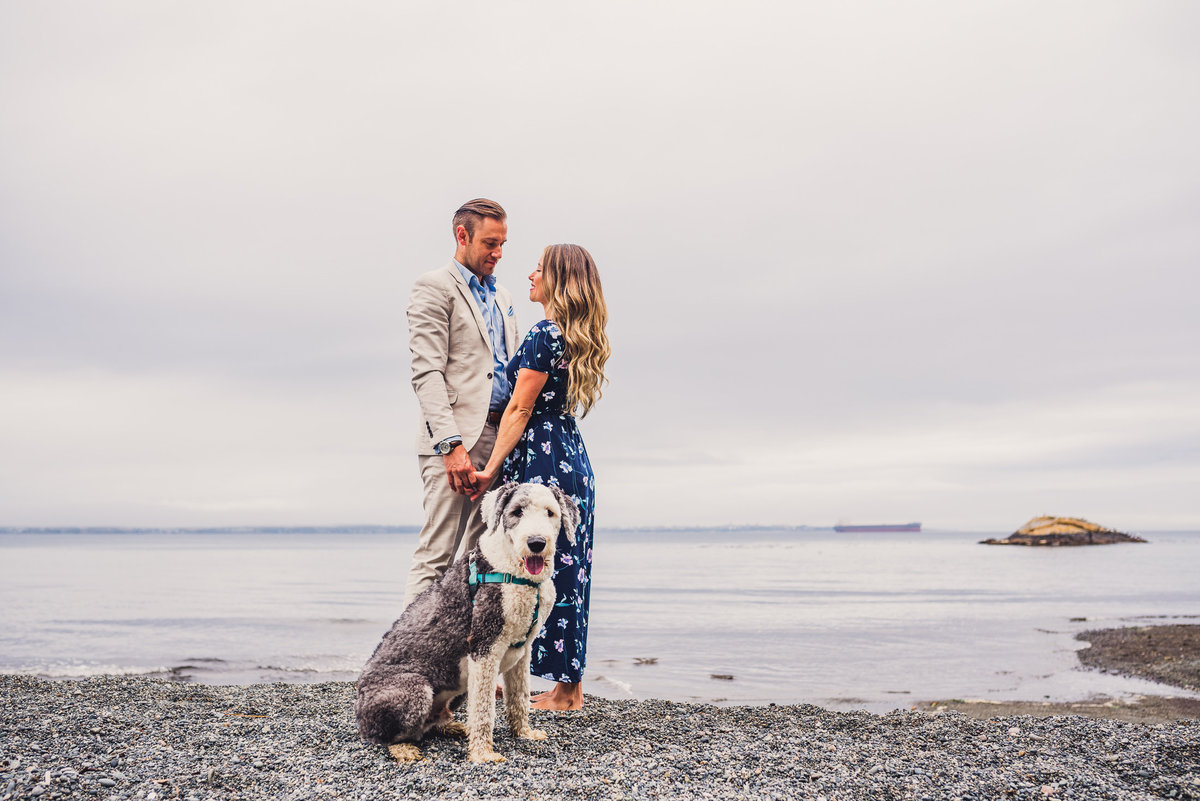 Dog smiling at camera with couple and ocean in background