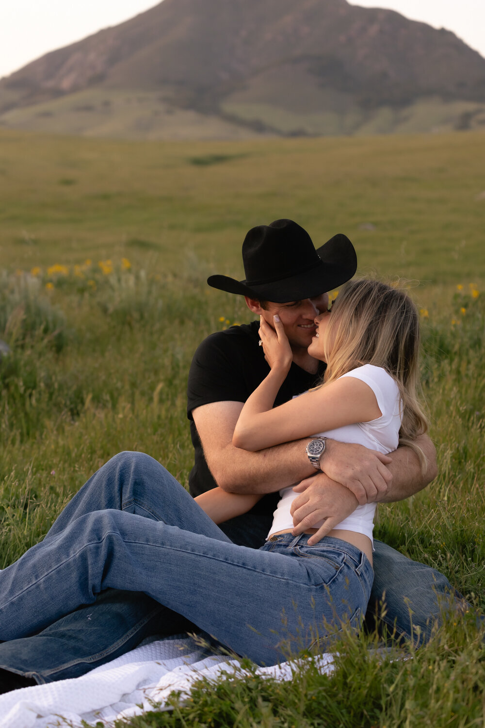 Candid couple sitting laying during engagement photos in  field with hills San Luis Obispo on the Central Coast 
