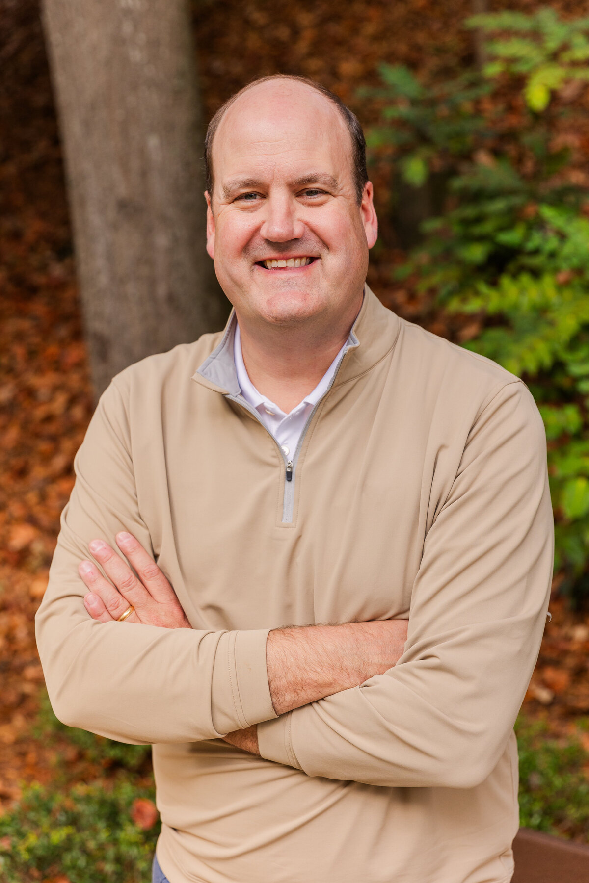 man wearing a white shirt and a beige sweater standing arms crossed facing the camera in a park during portraits session