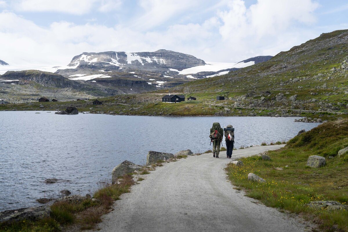two backpackers hike next to a lake in norway