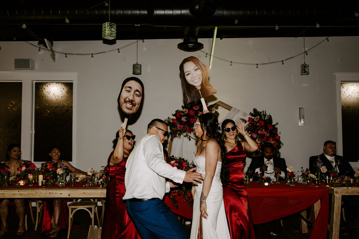 The wedding couple dances while friends hold giant posters of their faces.