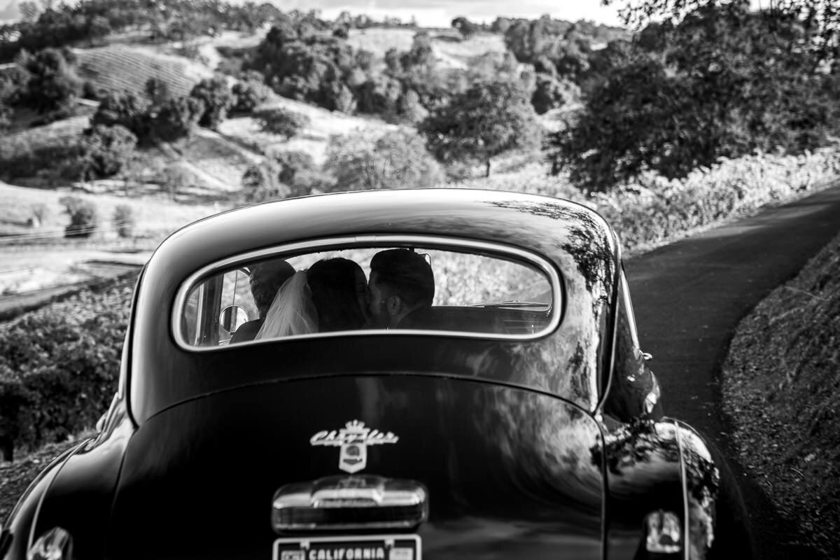 A timeless moment captured at Airola Road Vineyards in Murphys, California, as the bride and groom share a joyful ride in a vintage classic car, leaving their ceremony surrounded by scenic vineyard views. Perfect wedding photography showcasing elegance and charm in Northern California.