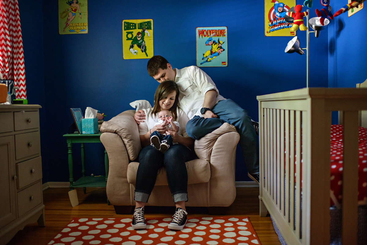 New parents hold their baby in the nursery filled with comic book characters.