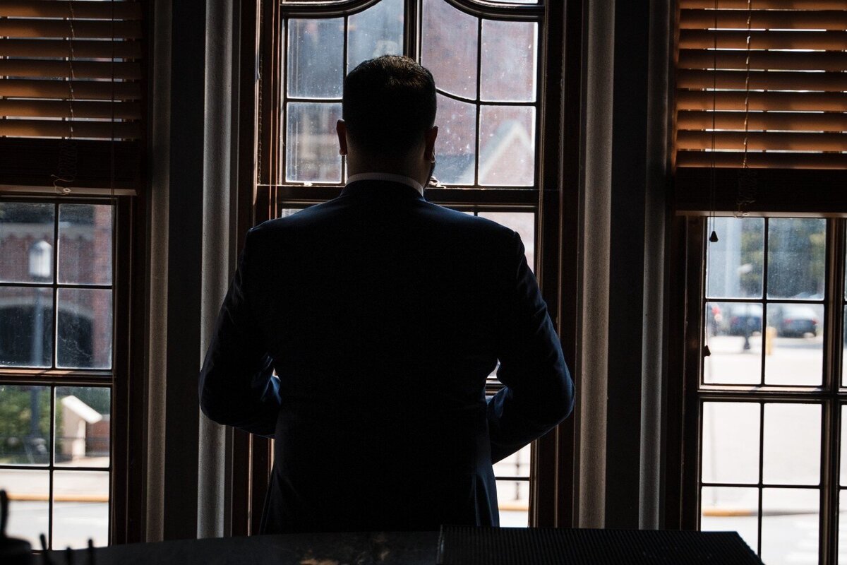 Groom silhouetted in front of window with city view at Union Club Hotel.