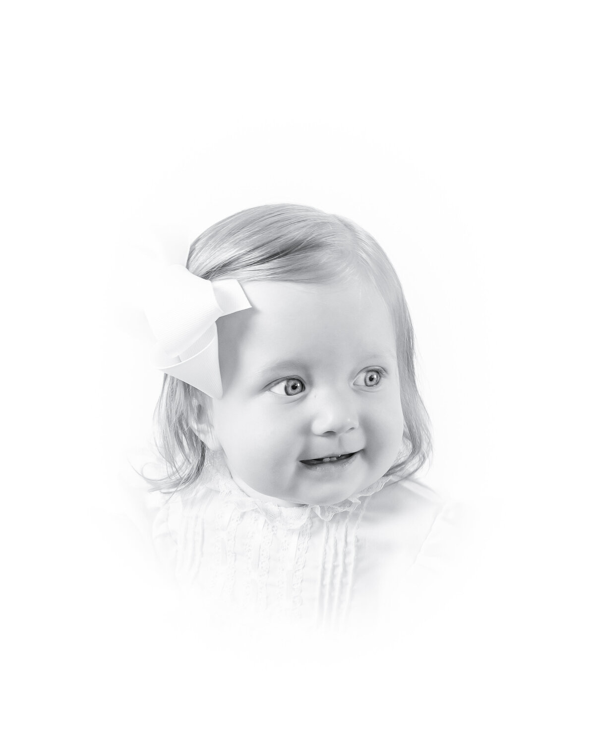 Black and white heirloom portrait of a smiling baby dressed in a classic white outfit with lace details. This timeless baby photography captures the innocence and joy of childhood, created by a Birmingham newborn photographer specializing in elegant, light-filled portraits.