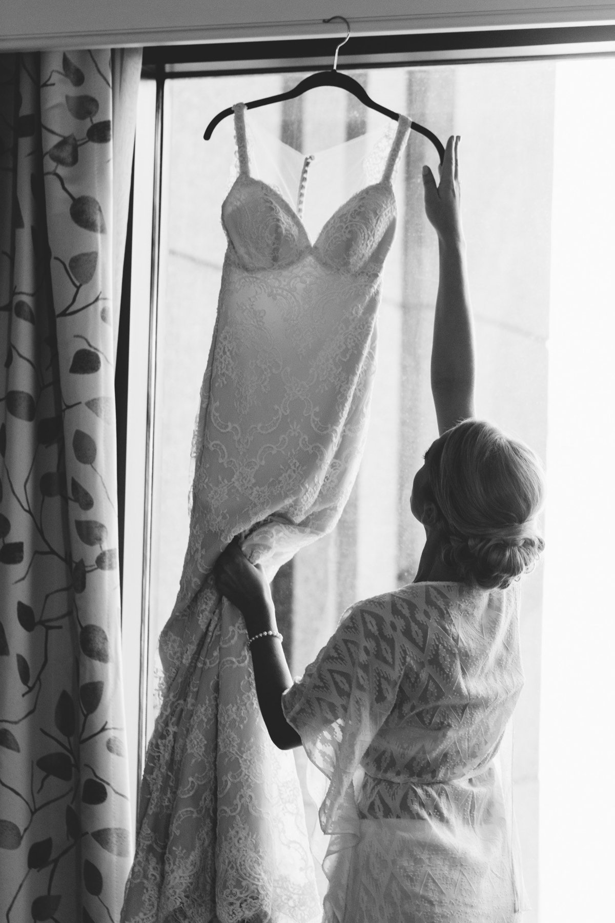 Dressed in a pretty bride robe, Tracy reaches for her lace wedding gown.   Real moment captured by Atlanta based photographer Rebecca Cerasani.