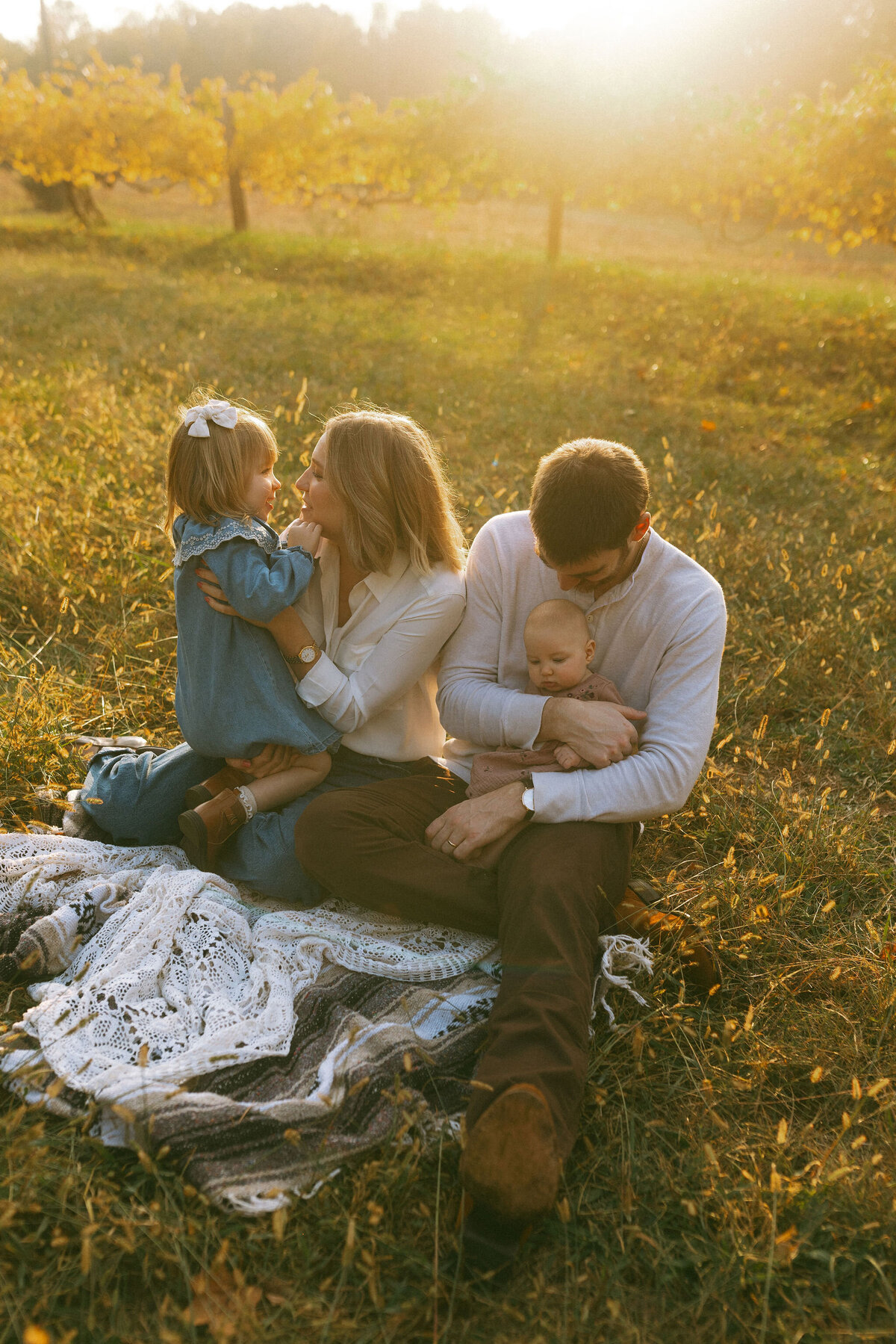 A family of four sitting on a blanket during golden hour at Hyde Farm Park. 