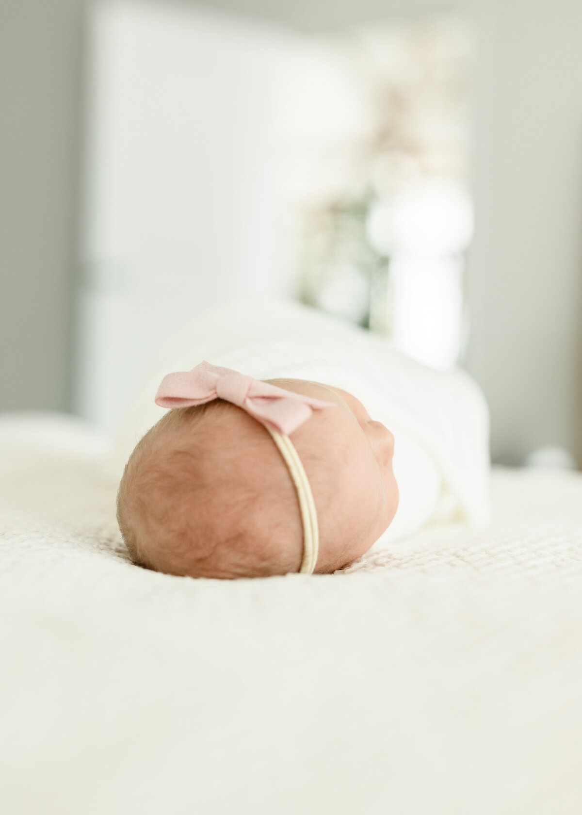 Swaddled newborn baby lying peacefully on a soft cream surface, wrapped in a dusty pink wrap.