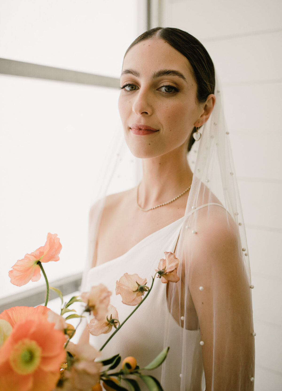 Bride wearing sleek white dress holding bouquet of white orange and yellow florals