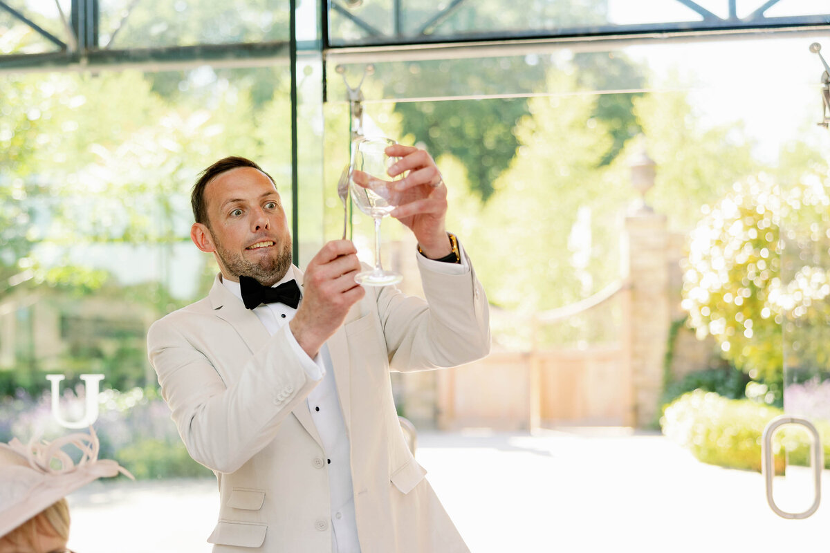 Groom wearing a white tux jacket cheekily clicking his glass