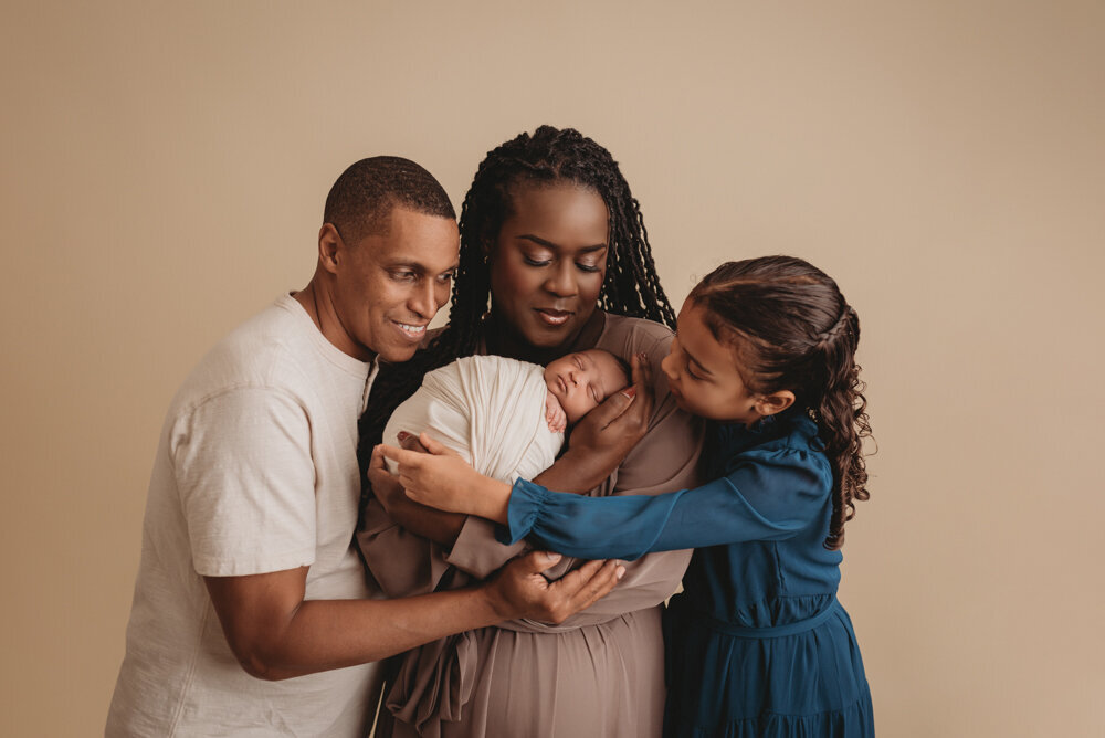 Newborn photos with Atlanta, Georgia newborn photographer of sleeping baby boy with hands under chin wrapped in cream swaddle being held by his mom, dad and big sister.