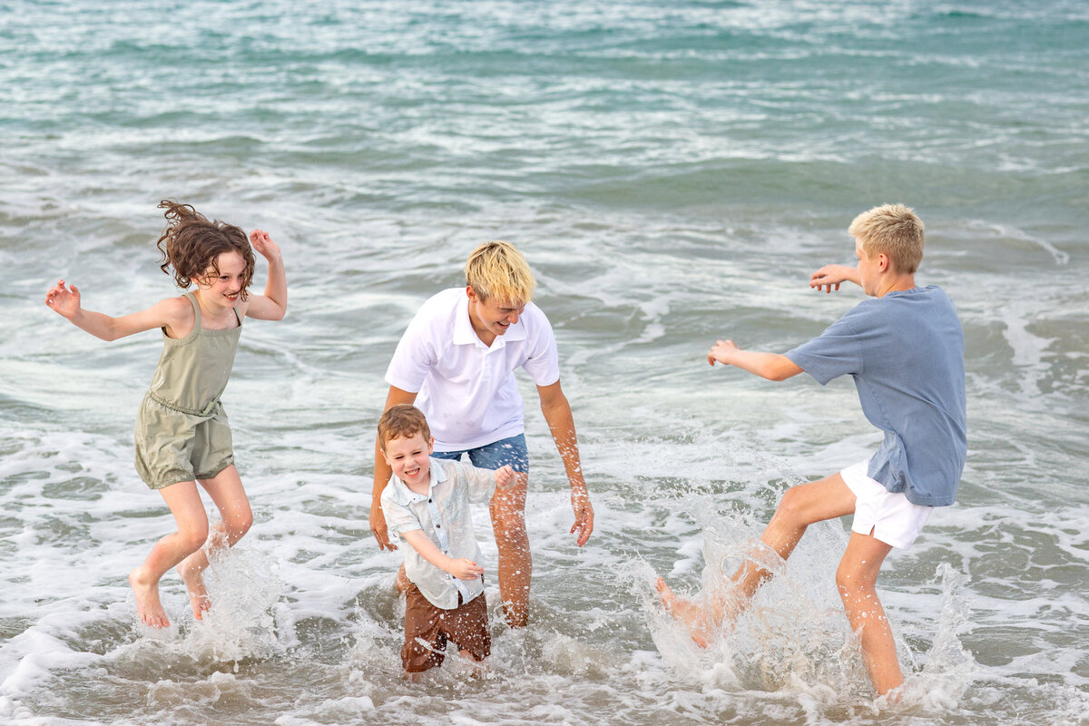 kids wearing green white and blue splashing in the ocean smiling during a family photoshoot
