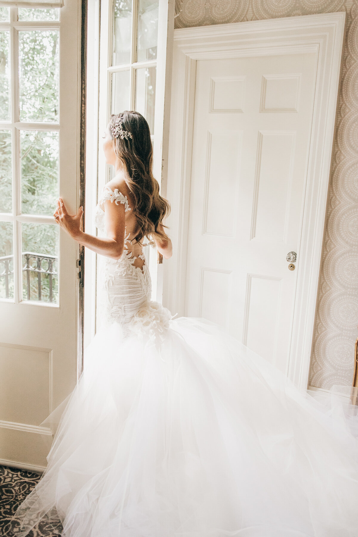 Glamorous portrait of bride looking out french doors on her wedding day