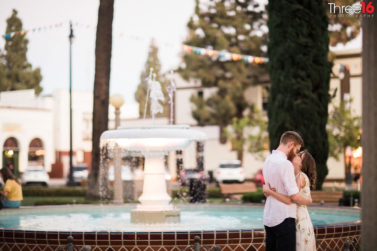 Engaged couple fully embrace one another in front of the water fountain in Old Towne Orange