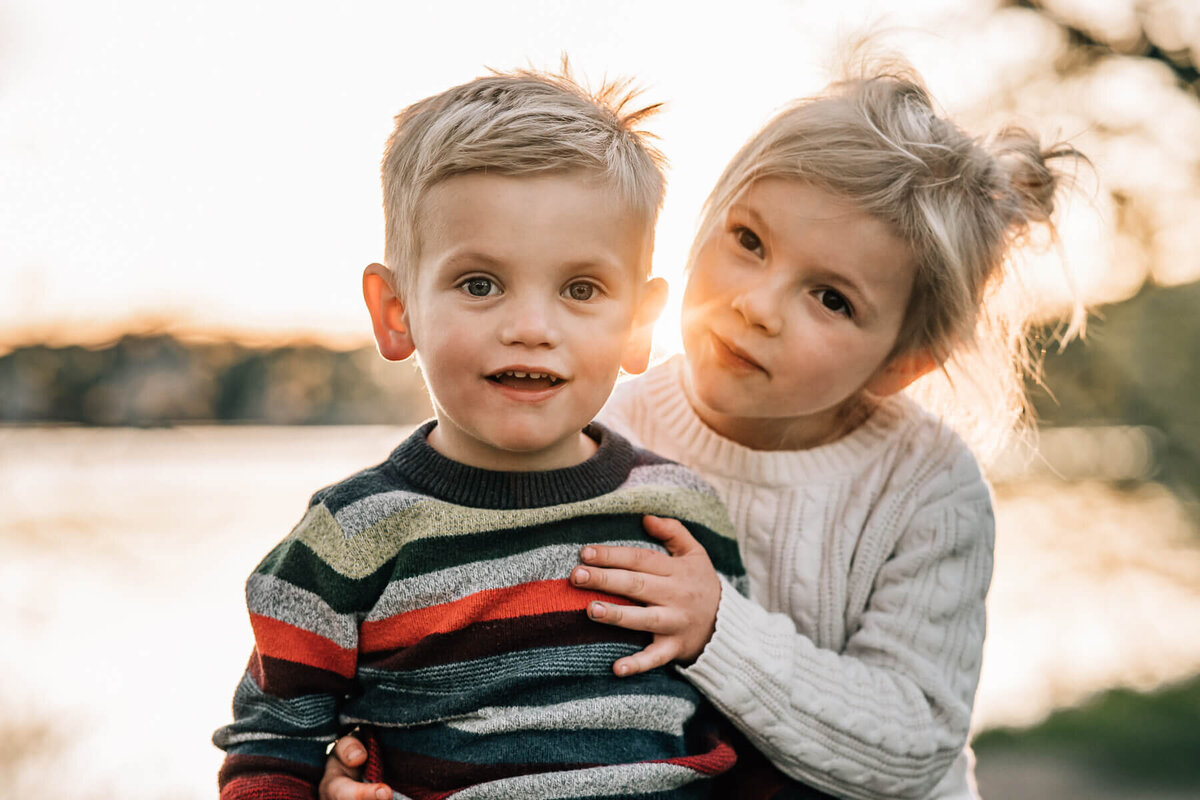 A little girl sits next to her brother and hugs him at Lake Harriet in Minneapolis during a family photoshoot.