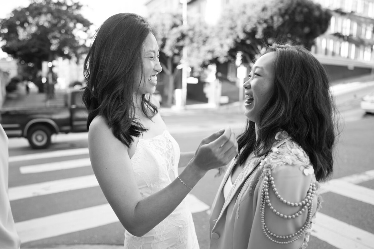 Black and white portrait of queer lesbian brides in San Francisco laughing with each other in the street