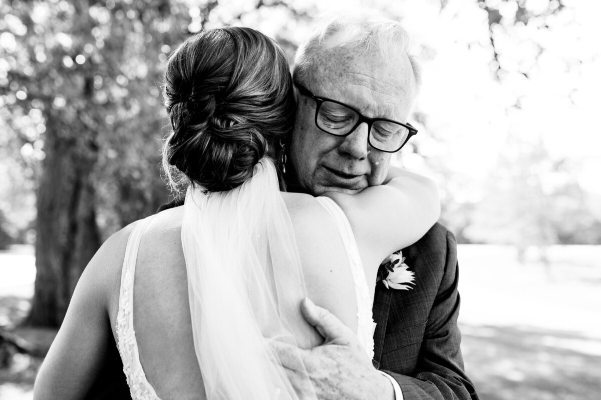 One of the top wedding photos of 2020. Taken by Adore Wedding Photography- Toledo, Ohio Wedding Photographers. This photo is of a father crying with tears rolling down his face hugging his daughter before the wedding at Nazareth Hall in Toledo Ohio