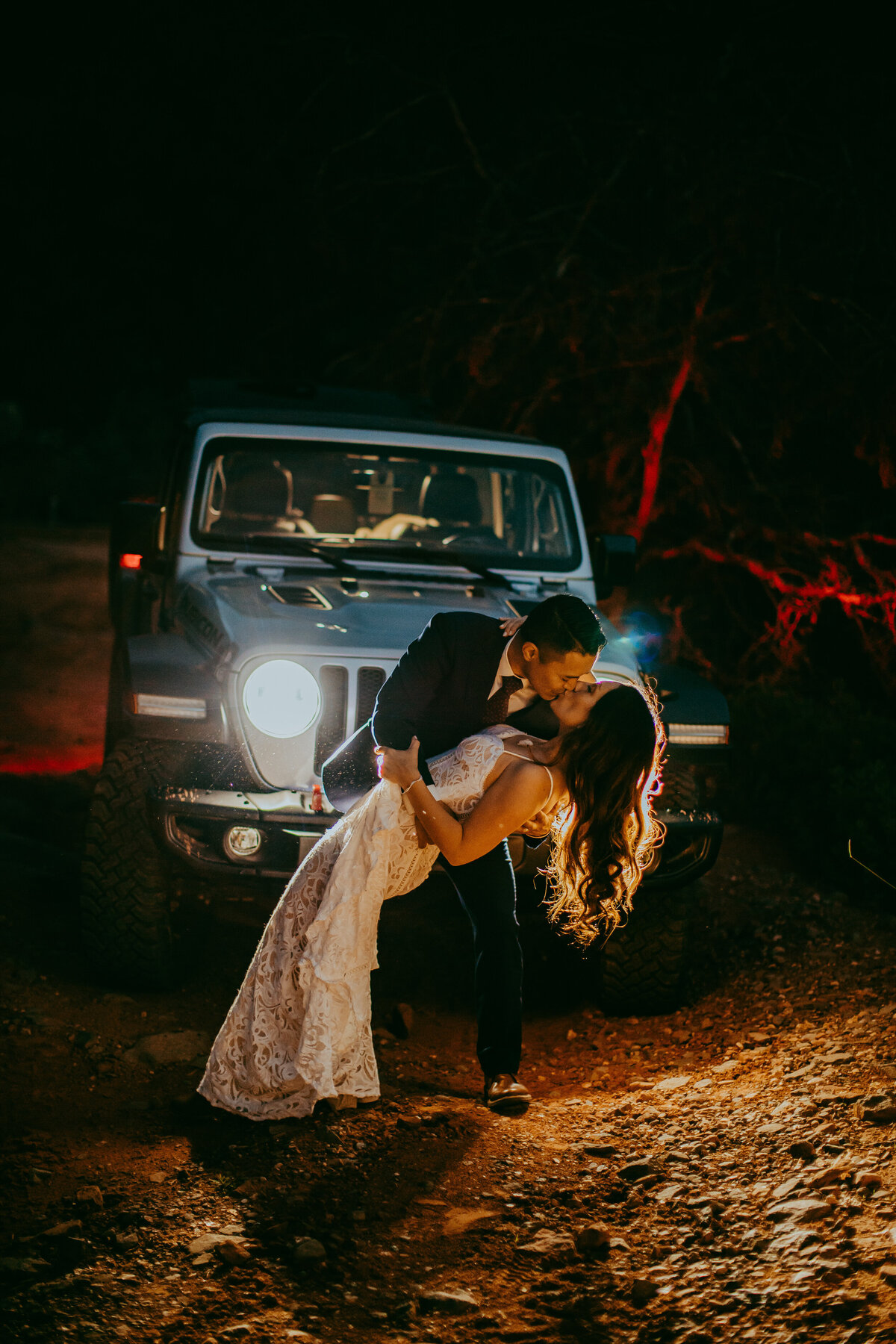 couple dipping with a kiss in front of jeep headlights