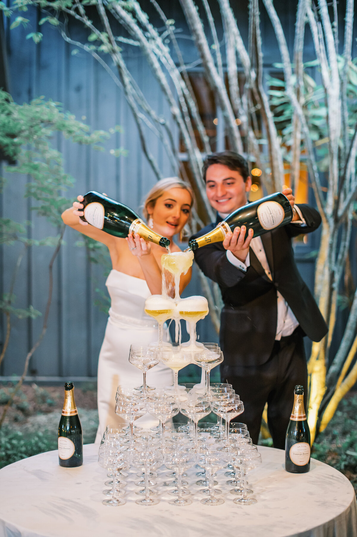 Bride and groom pour champagne into a coupe glass tower during their wedding celebration at Old Edwards Inn in Highlands, North Carolina.