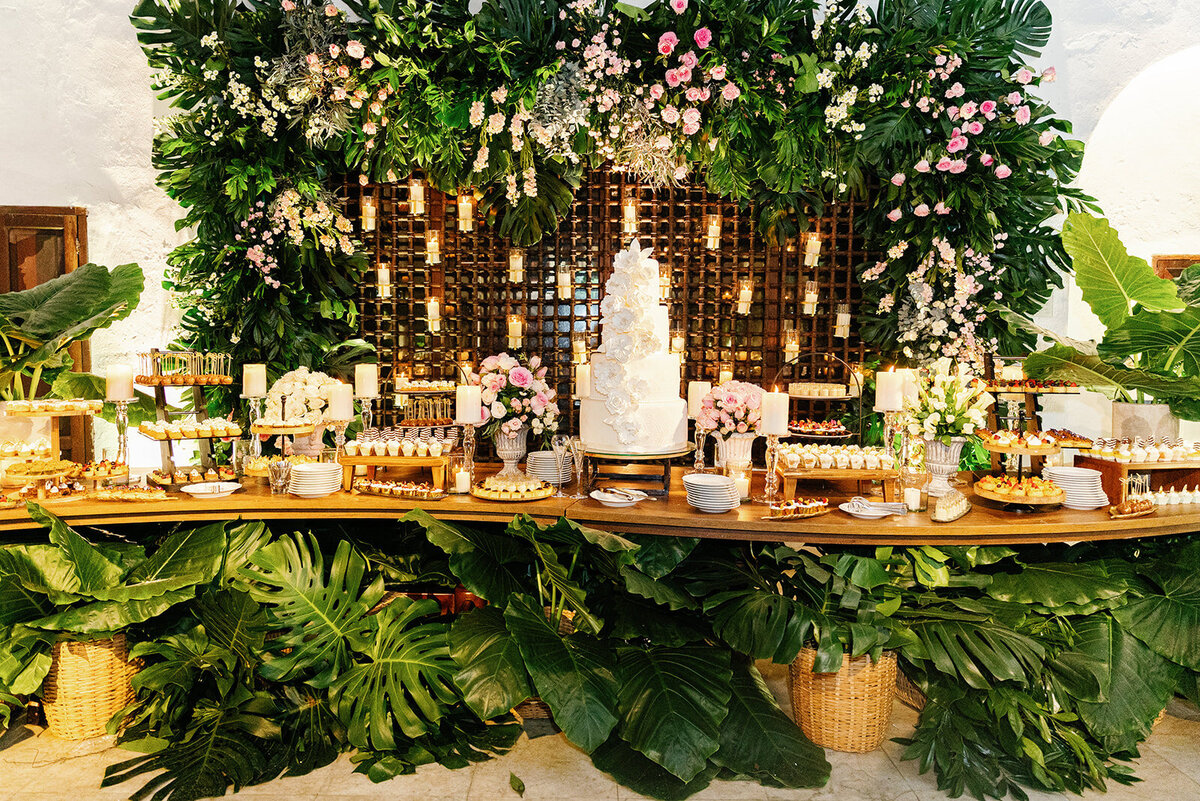 A lavish dessert table setup with an elegant wedding cake, floral arrangements, and candlelit decor at Victoria and Daniel’s Cartagena wedding.