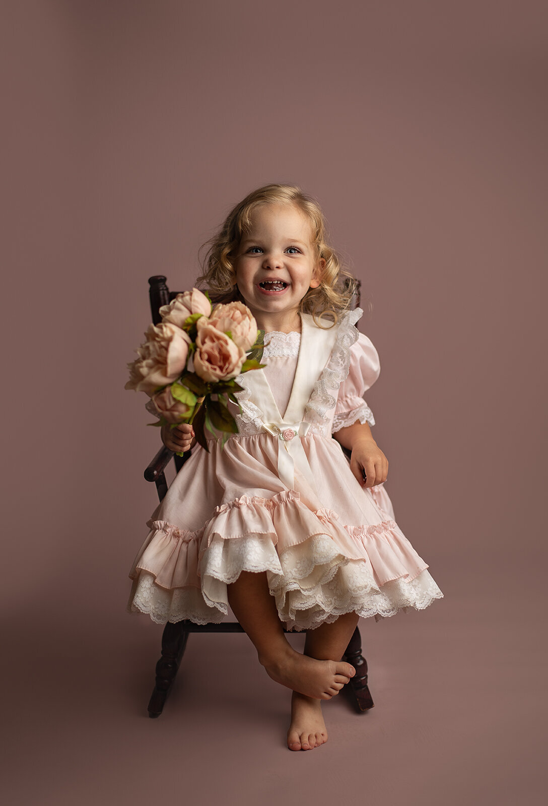 girl in pink dress sitting in rocking chair smiling with flowers