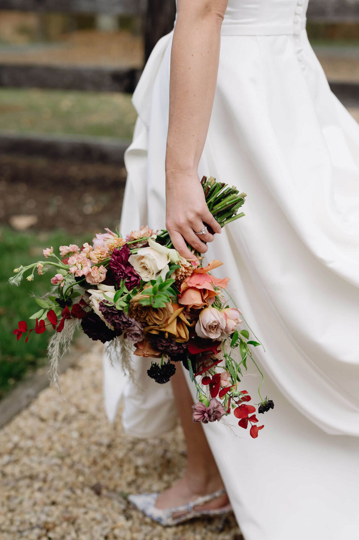 detail shot of bride holding a red and purple autumn wedding floral bouquet to her side as she walks through the venue
