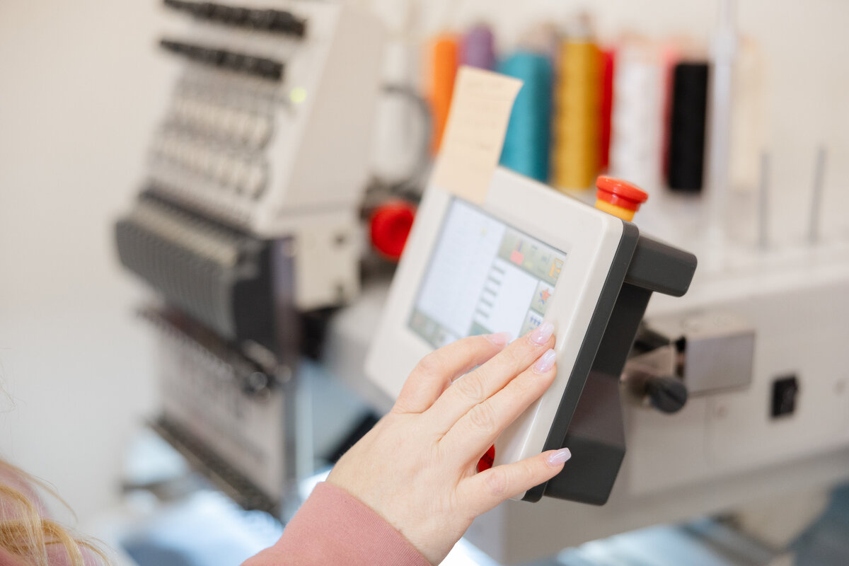 Close-up of hands holding embroidery thread samples in front of machine. Photograph by Yucaipa branding photographer Kaitlyn Dawn Photography.