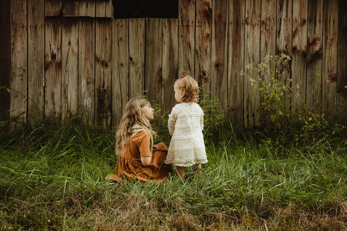Two sisters are talking amongst each other near a barn.