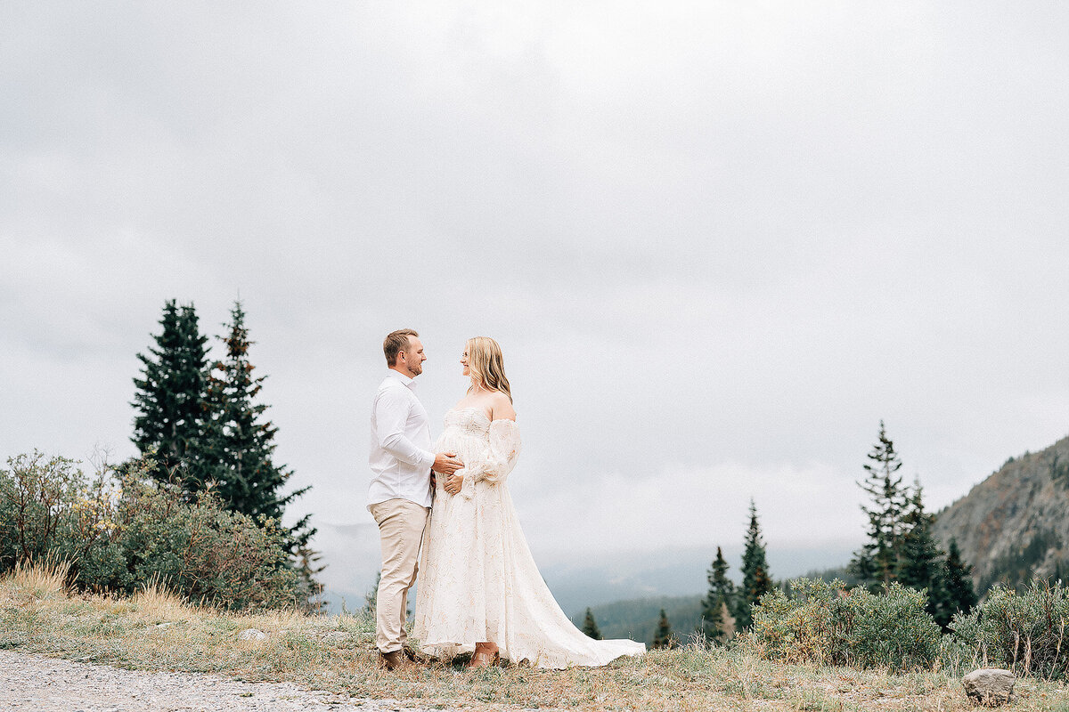 couple at the top of the mountain with their hands on mother's pregnant belly