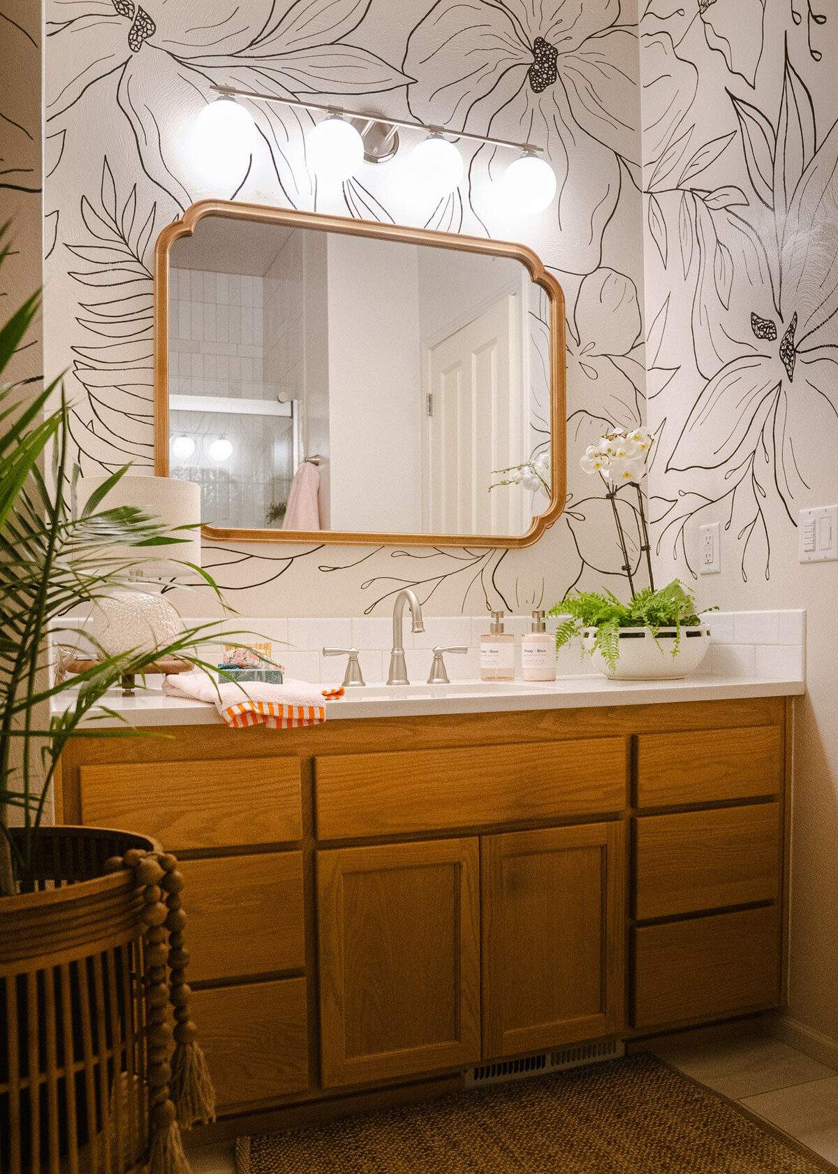 A bathroom vanity with a mirror and plant featuring a wall with modern florals hand painted on it representing full service design and calligraphy by Life in Letters.