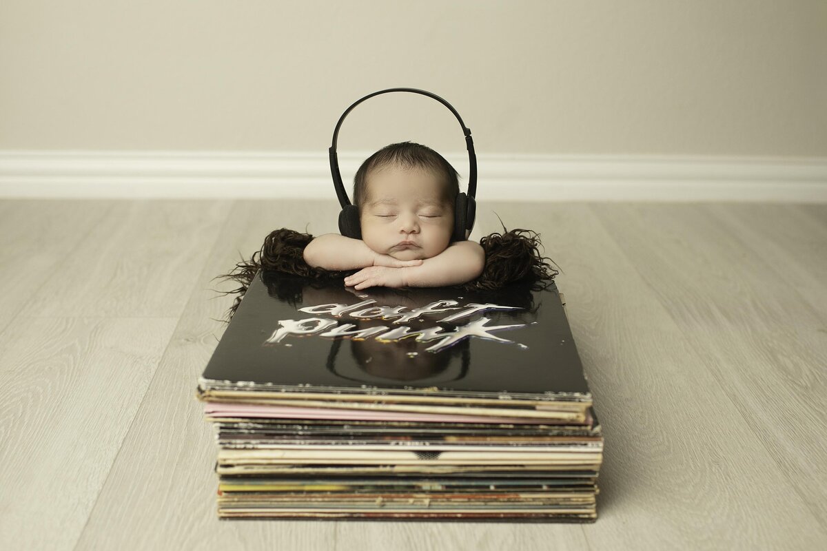 Newborn baby peacefully lying on top of a collection of vinyl records, wearing tiny headphones, creating a unique and adorable music-inspired scene