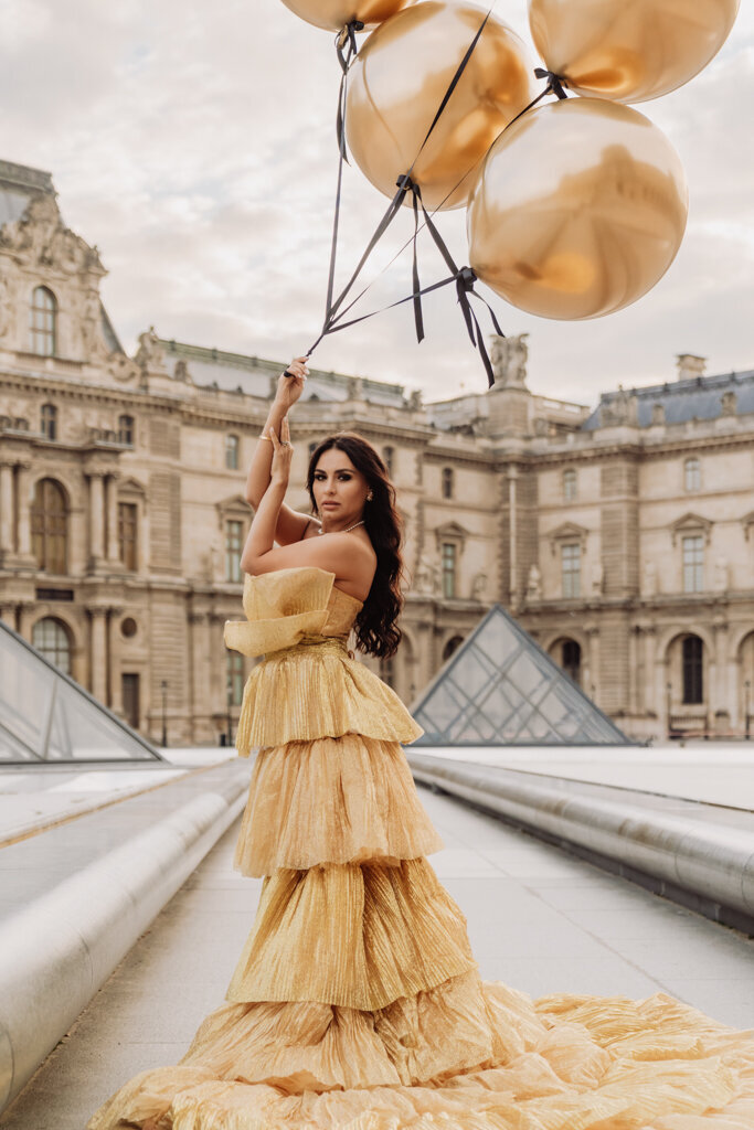 Luxury portrait photoshoot at Louvre courtyard with woman in gold princess dress holding golden balloons