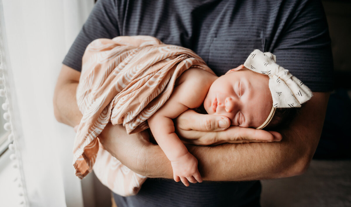 Newborn Photographer, a baby girls lay sleeping in her fathers arms