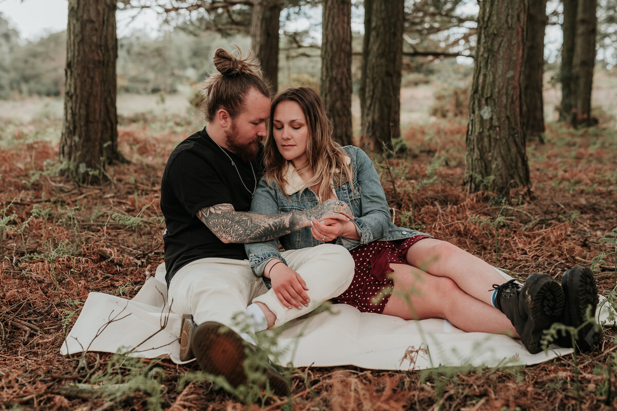 Lovely couple sit together on cosy blanket enjoying a picnic in the woodlands in Brockenhurst, New Forest