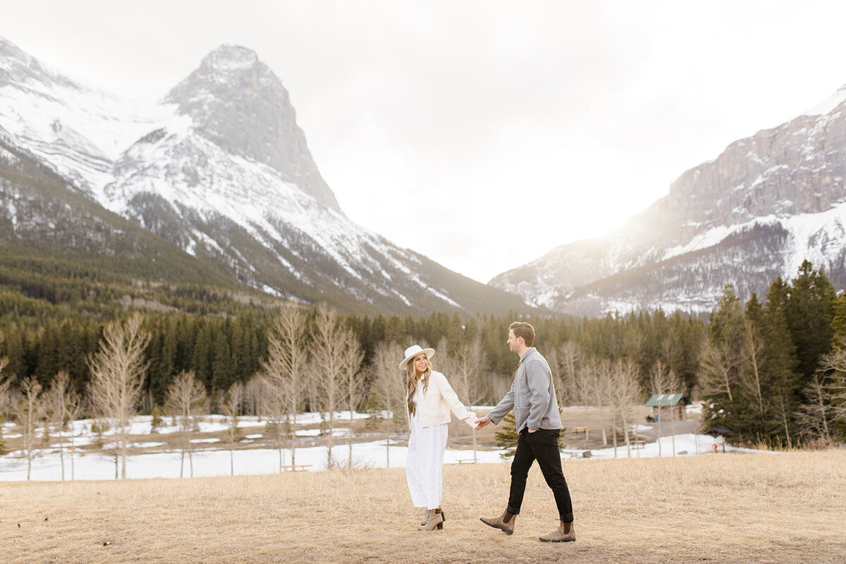 Woman turns to look at man whose hand she is holding during an engagement photoshoot in the Rocky Mountains
