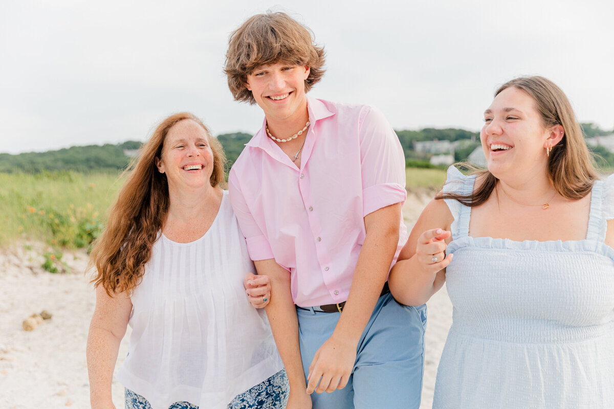 A mom and her two grown children laugh while walking on a Cape Cod beach together