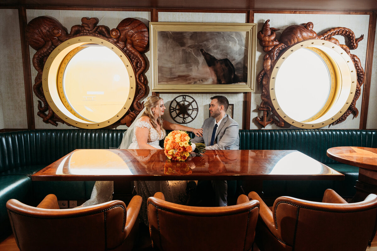  Bride and groom sit inside the nautical Crackin’ Lounge aboard the Disney Wish, surrounded by octopus-framed portholes and rich wood textures.