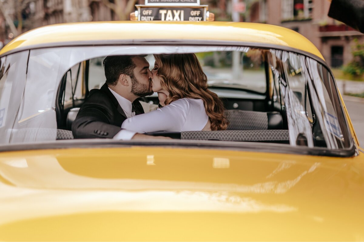Bride and Groom sharing a kiss in a vintage taxi with the photo shot  from behind the taxi.