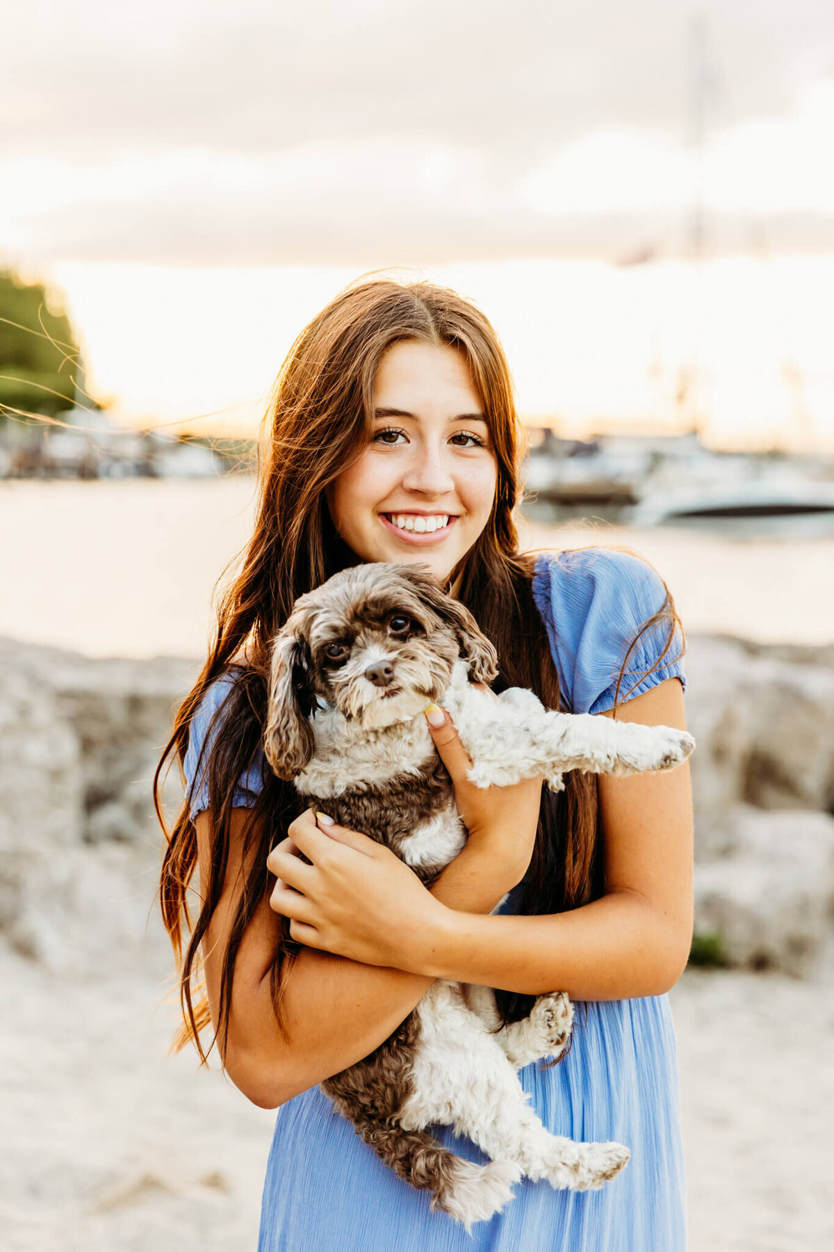adorable portrait of a teen girl holding her dog as she smiles while standing on the beach