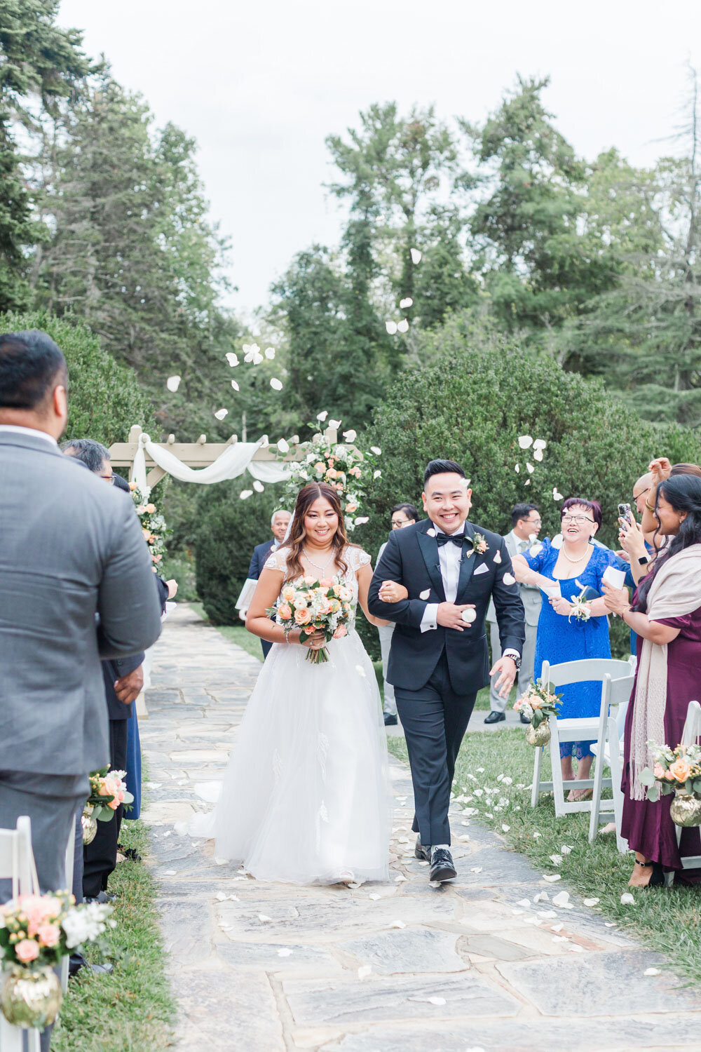 Bride and groom walking down the aisle and guest tossing flowers on them